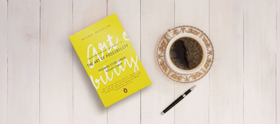 Photo of "The Art of Possibility" book on a white wooden table next to a cup of coffee and a pen