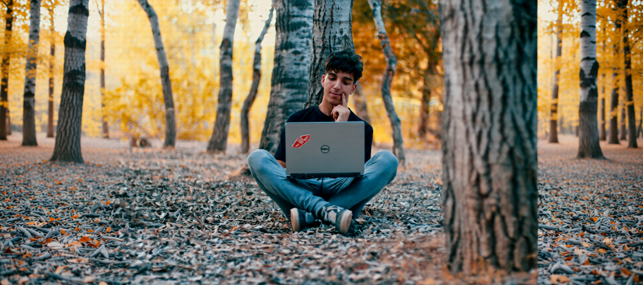 Photo of a man sitting in the woods, contemplating what he's looking at on his laptop. Photo by Hamza Tighza.