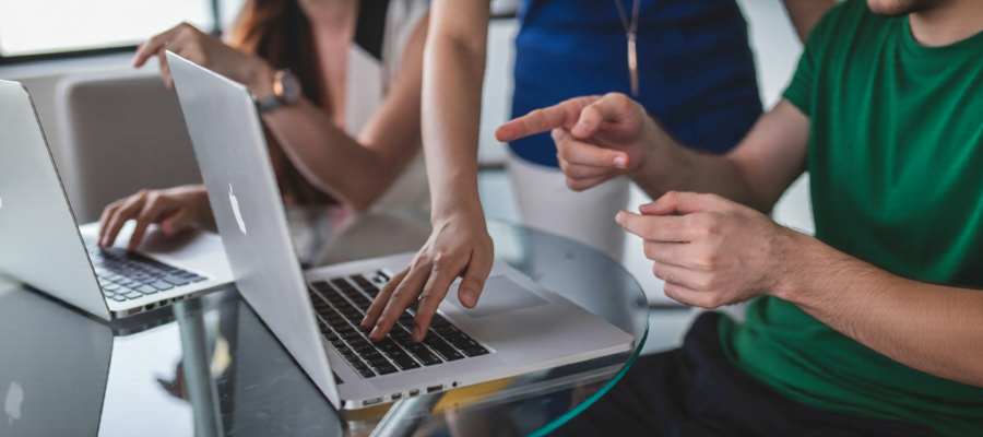 Close up of three people's hands as they use two laptops at a glass table