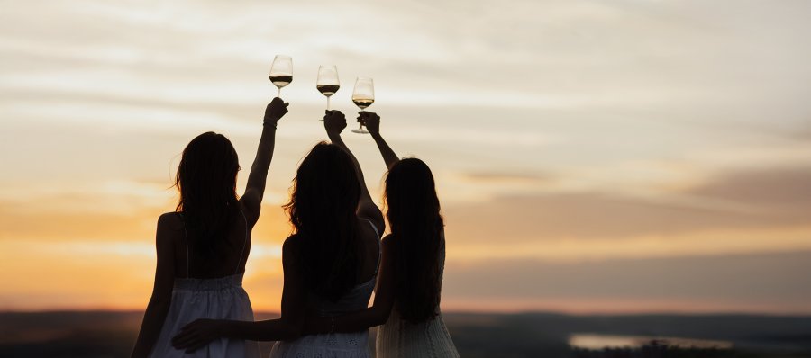 Photo of three women holding up wine glasses silhouetted by a sunset at dusk