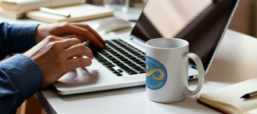 Close-up photo of a person's hands as they use their laptop. Next to the laptop is a coffee mug with an "infinity peanut" logo printed on the side