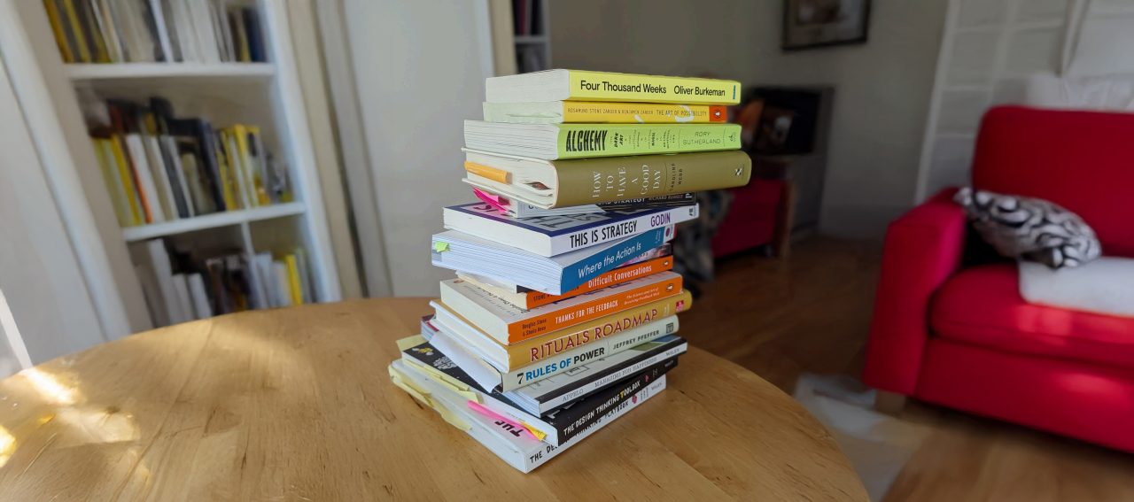 Image of a stack of books sitting on a wooden table in a living room.