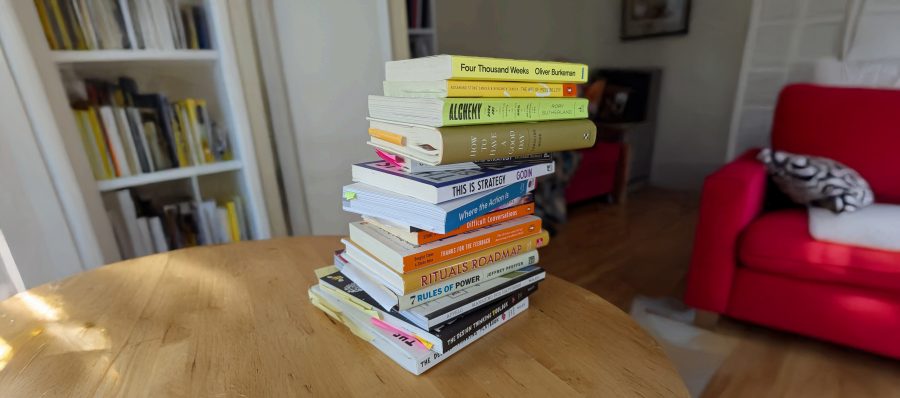 Image of a stack of books sitting on a wooden table in a living room.