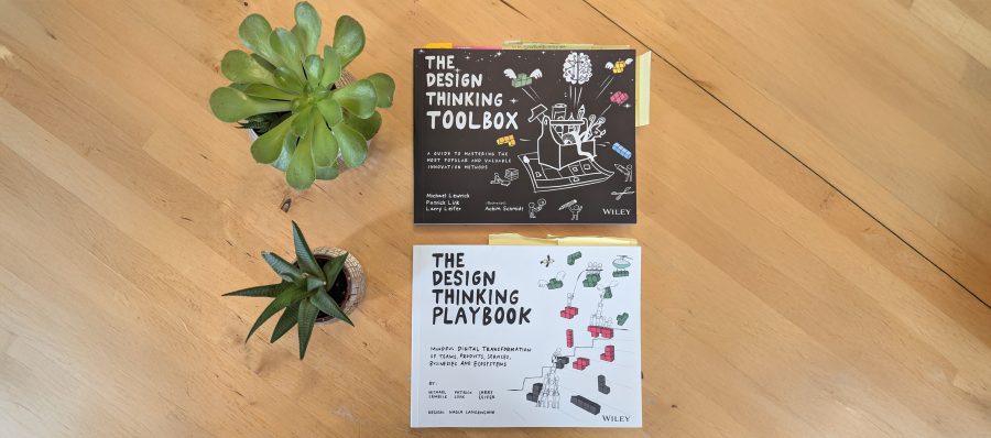 Photo of The Design Thinking Toolbox and The Design Thinking Playbook on a wooden table, next to two small houseplants